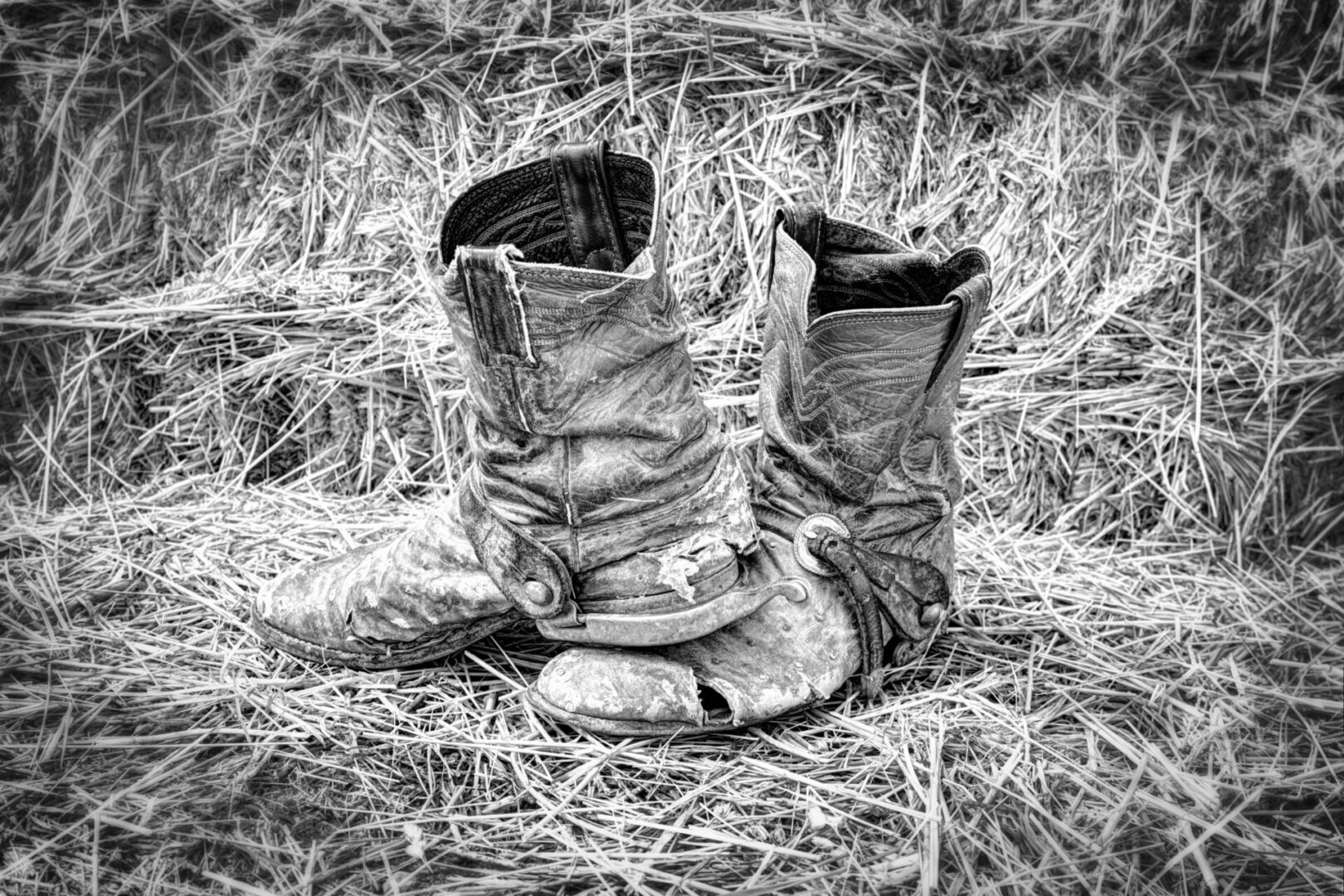 A pair of boots sitting on top of dry grass.