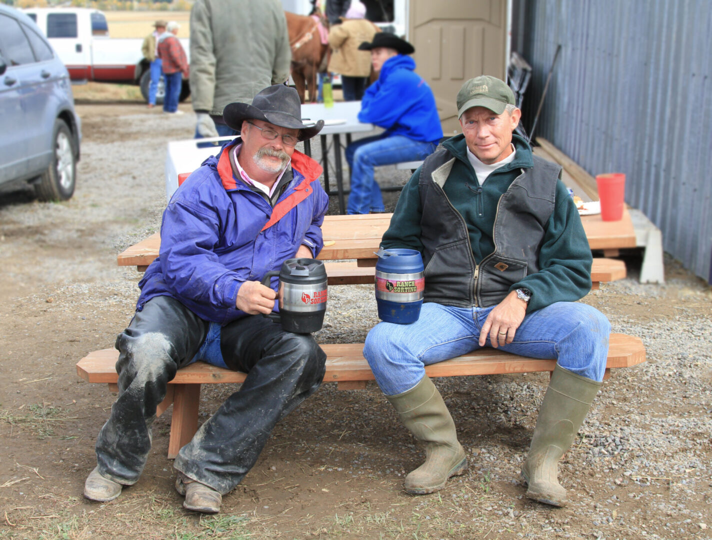 Two men sitting on a bench with cups of coffee.