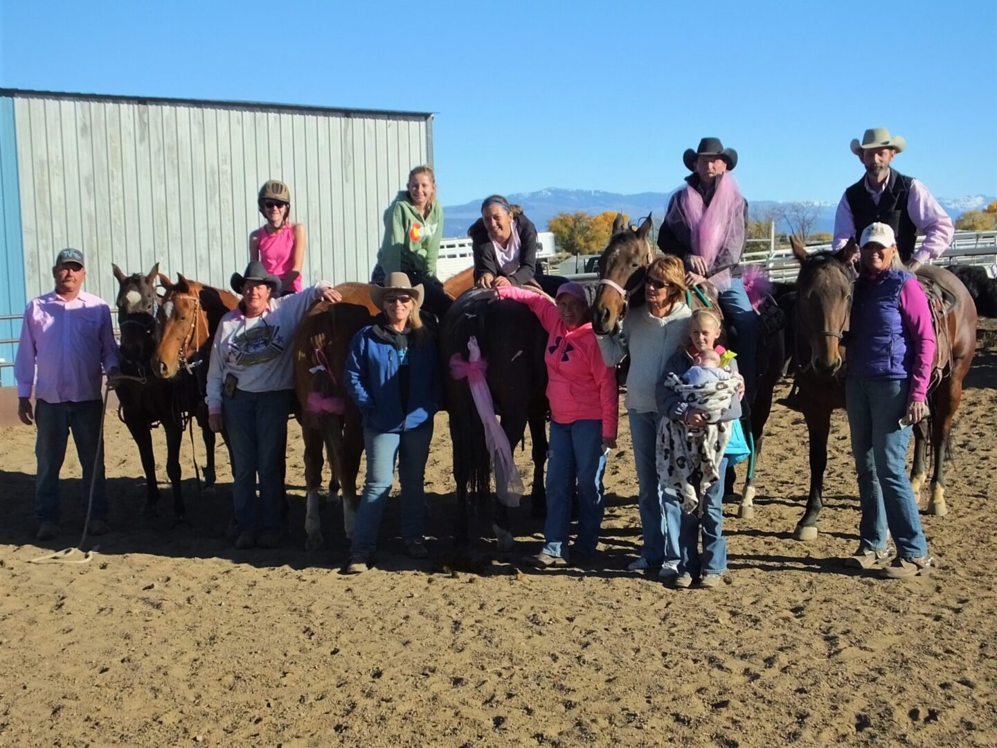A group of people standing around horses on dirt.