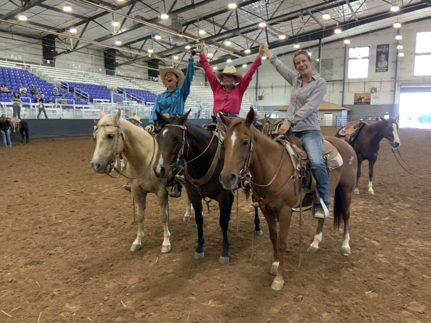 Three women riding horses in a dirt arena.